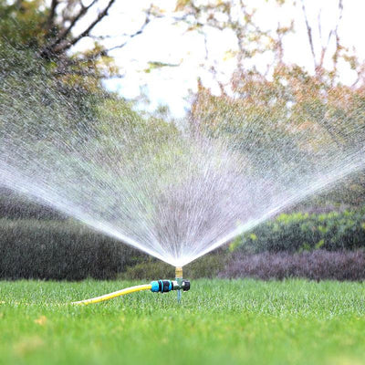Sprinkler spraying water on a grassy area with trees in the background