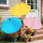 Three colorful umbrellas (yellow, blue, pink) held above potted flowers on a porch.