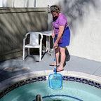 Woman cleaning a pool with a skimmer net on a patio.