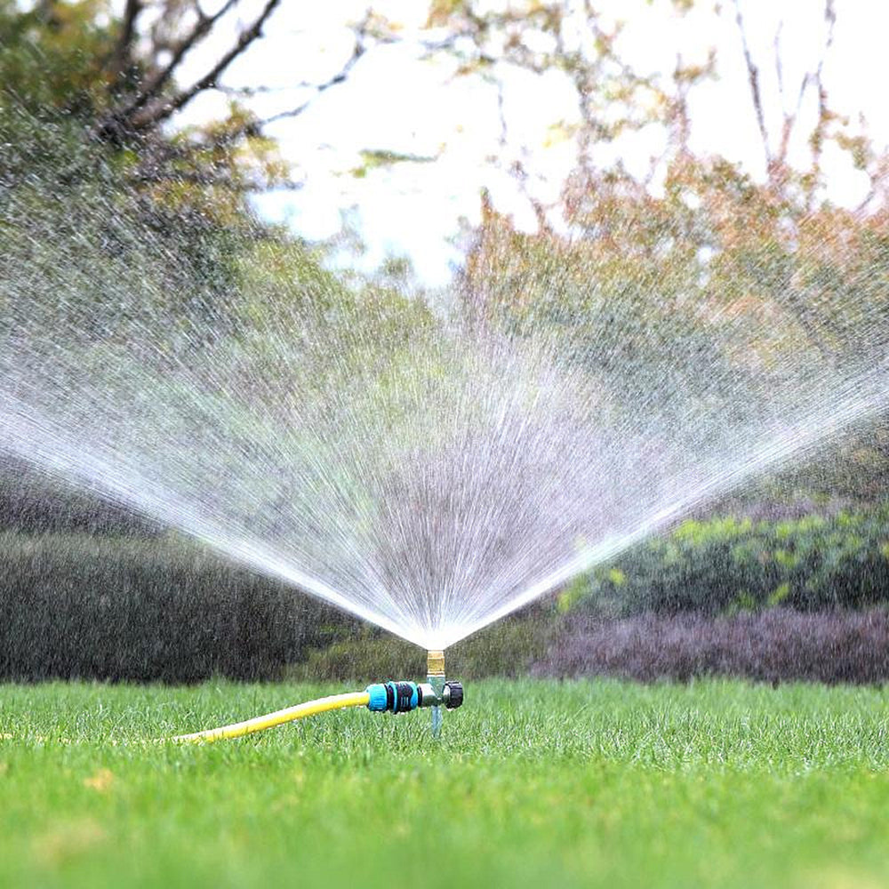 Sprinkler spraying water on a grassy area with trees in the background