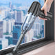 Hand using a handheld vacuum cleaner to clean a window with a cityscape in the background